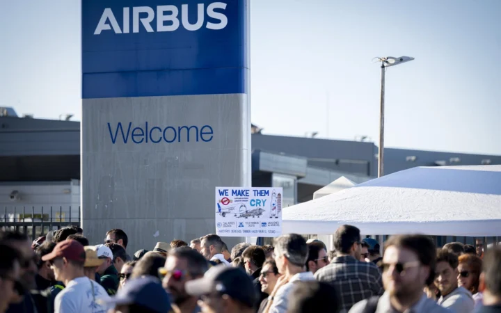 Fotografía editorial que muestra a trabajadores de Airbus concentrados frente a un cartel de bienvenida corporativo de la empresa durante una protesta laboral.