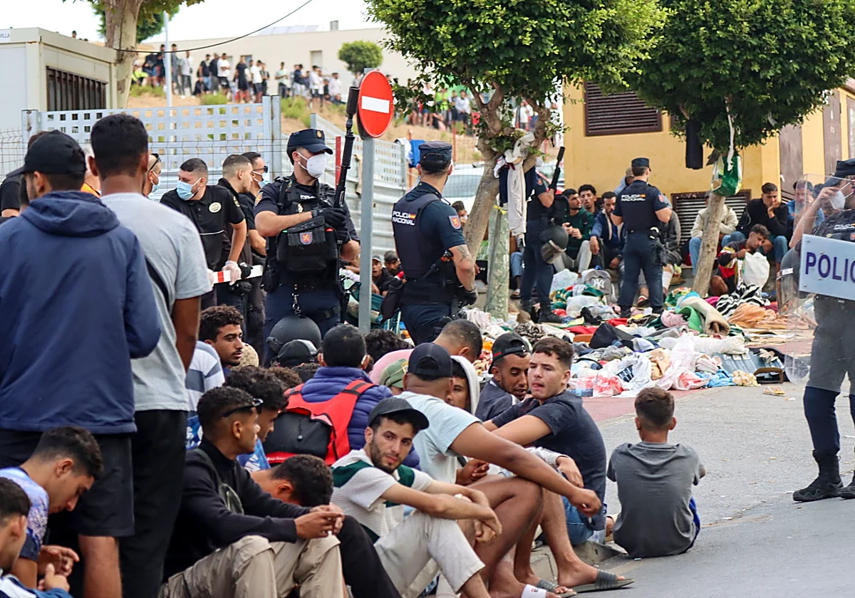Policías nacionales españoles controlando a migrantes sentados en el suelo durante una crisis migratoria fronteriza.