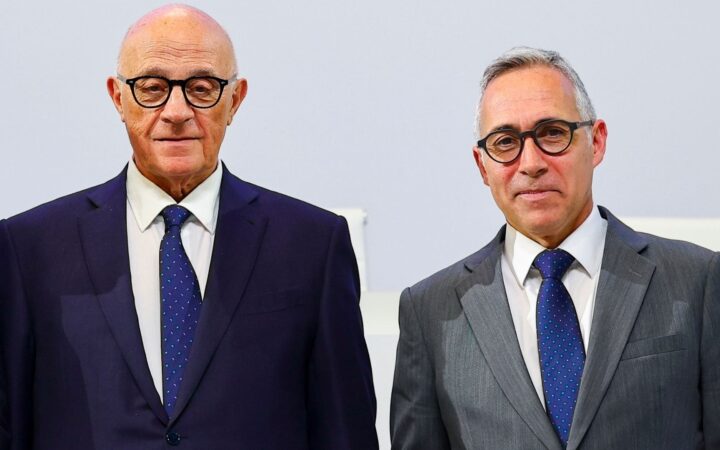 Fotografía editorial de dos ejecutivos bancarios trajeados con corbata y gafas mirando a cámara.