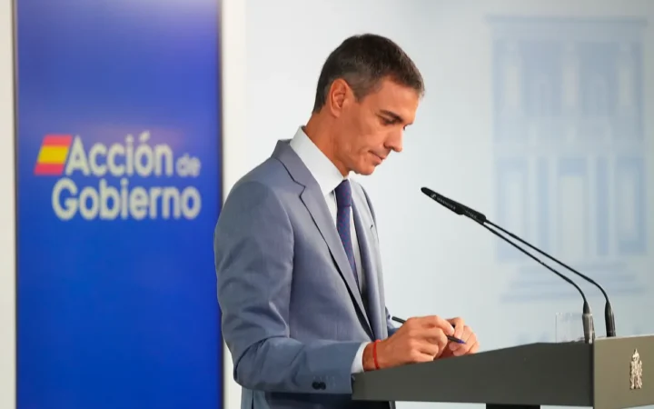 Fotografía editorial de Pedro Sánchez interviniendo en una rueda de prensa institucional con el logotipo de Acción de Gobierno de fondo.