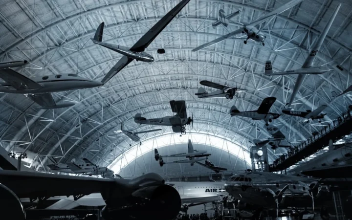 Fotografía de un museo aeronáutico con múltiples aviones históricos y planeadores colgados del techo en una gran estructura metálica abovedada.